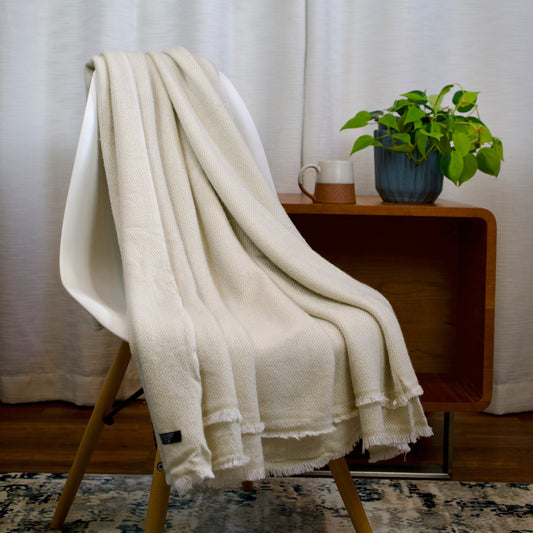 White cashmere blanket draped over a chair with a small table and plant in the background
