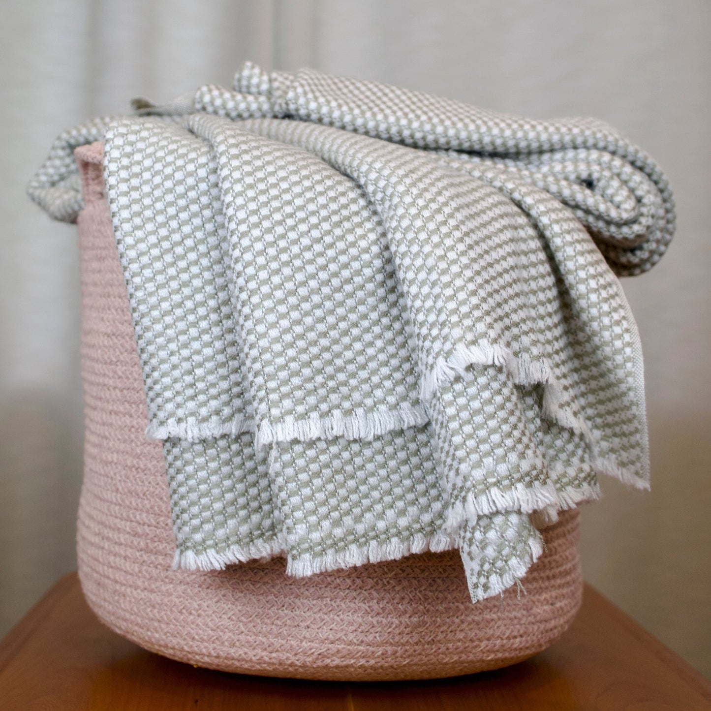 Grey Textured cashmere blanket draped over a woven basket 