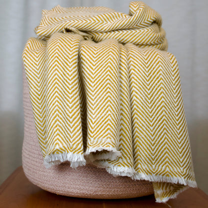 Golden Yellow chevron patterned blanket draped over a woven basket on a wooden surface with a neutral background