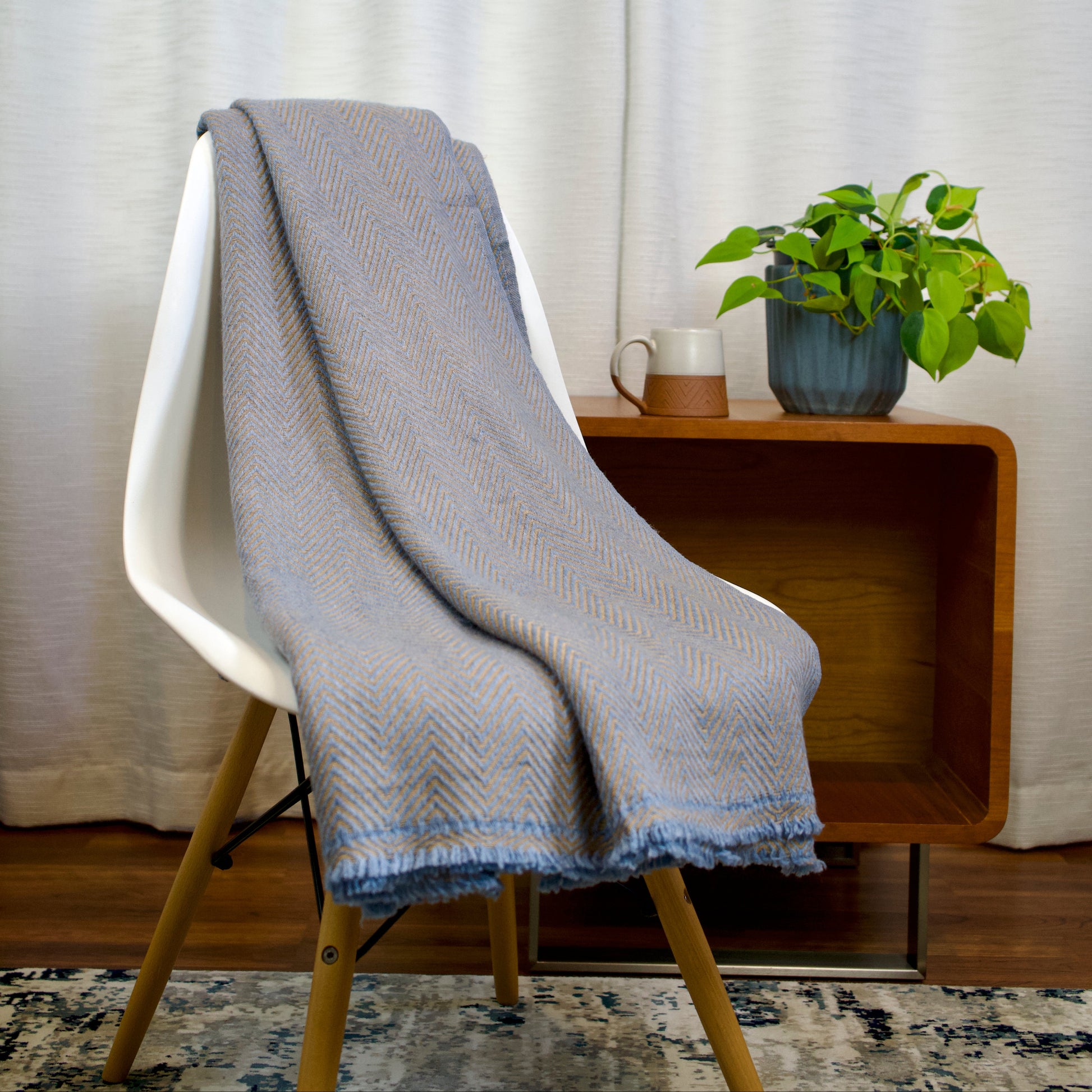 Blue and golden chevron blanket draped over a white chair with a wooden side table and plant in the background